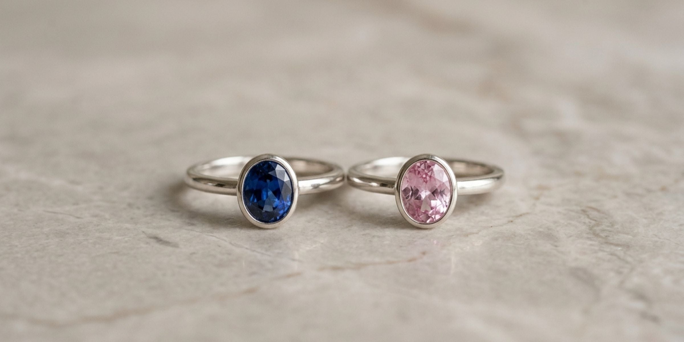 Sterling silver rings set with blue and pink sapphires side by side on marble
