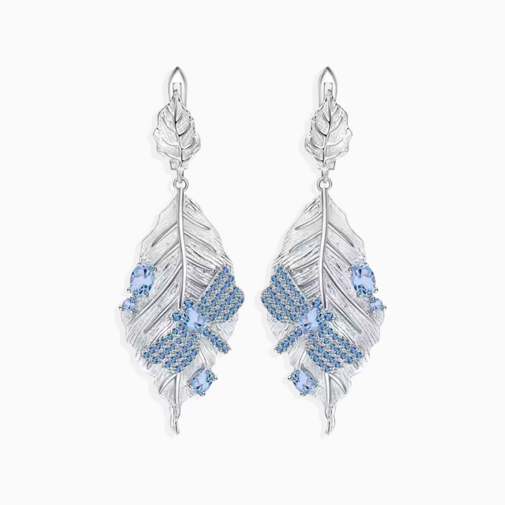 Silver feather-shaped dragonfly topaz earrings with blue gemstones on a white background