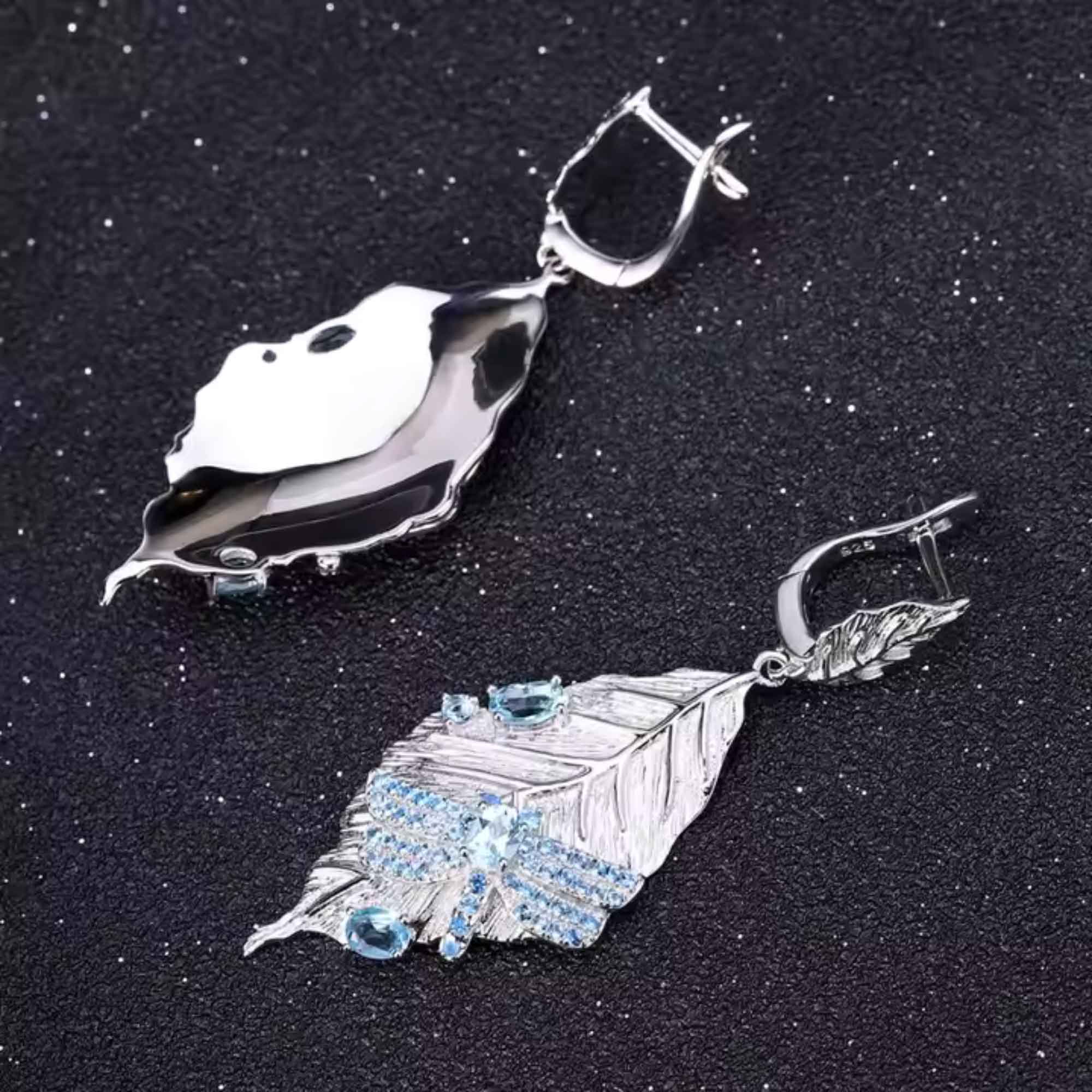 Silver leaf-shaped earrings with blue gemstones on a dark background