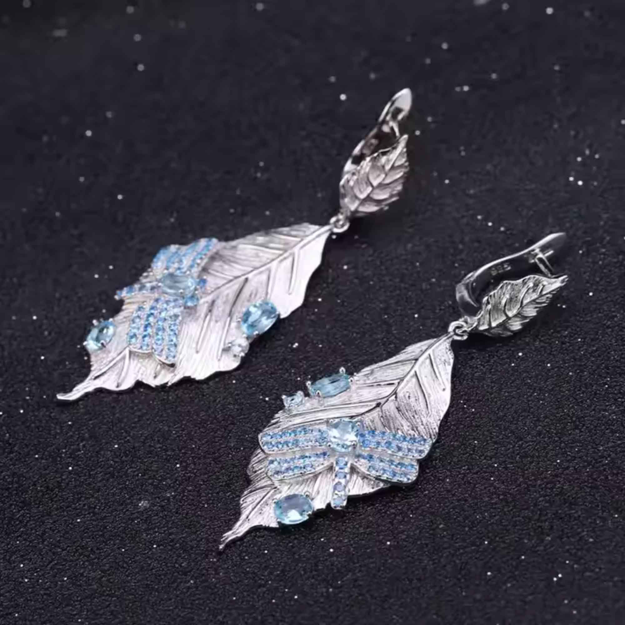 Silver leaf-shaped earrings with blue gemstones on a black background