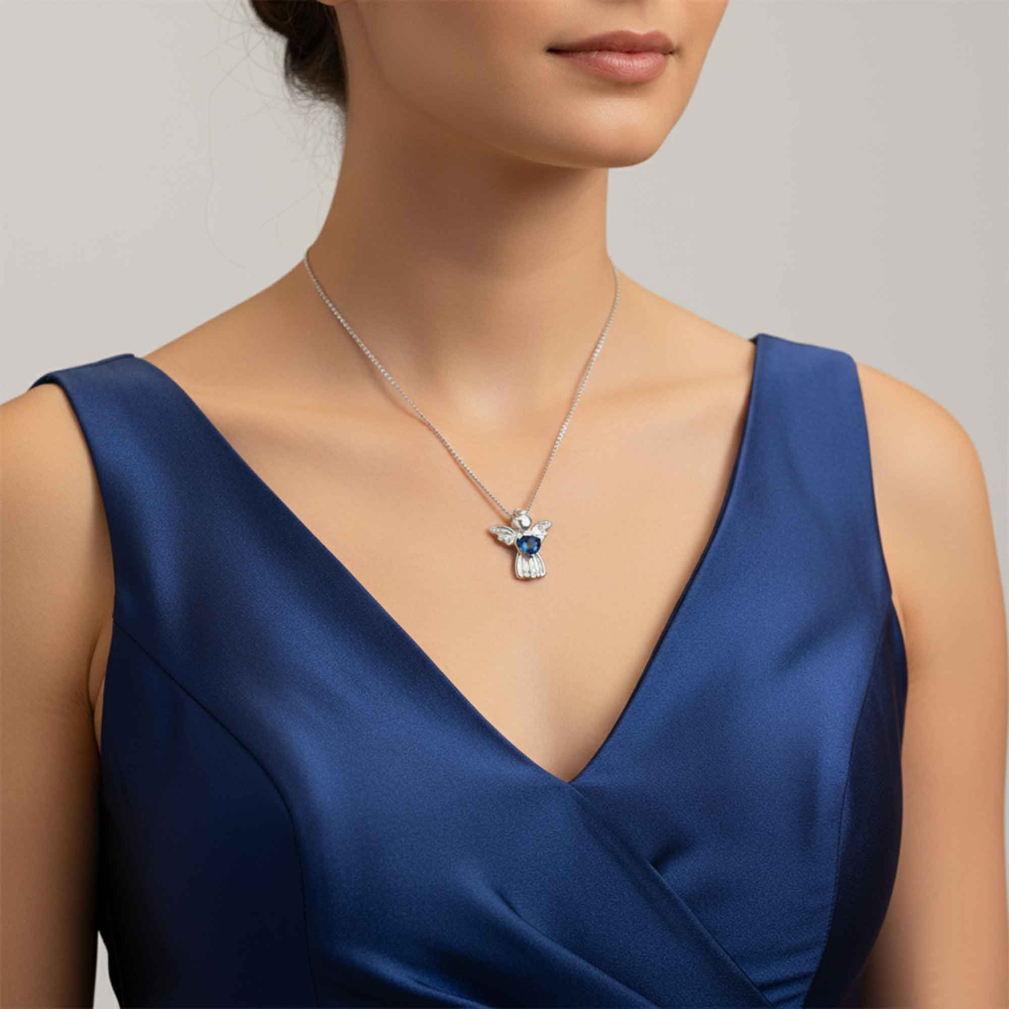 Woman wearing a blue dress with a silver necklace featuring a blue topaz gemstone pendant.