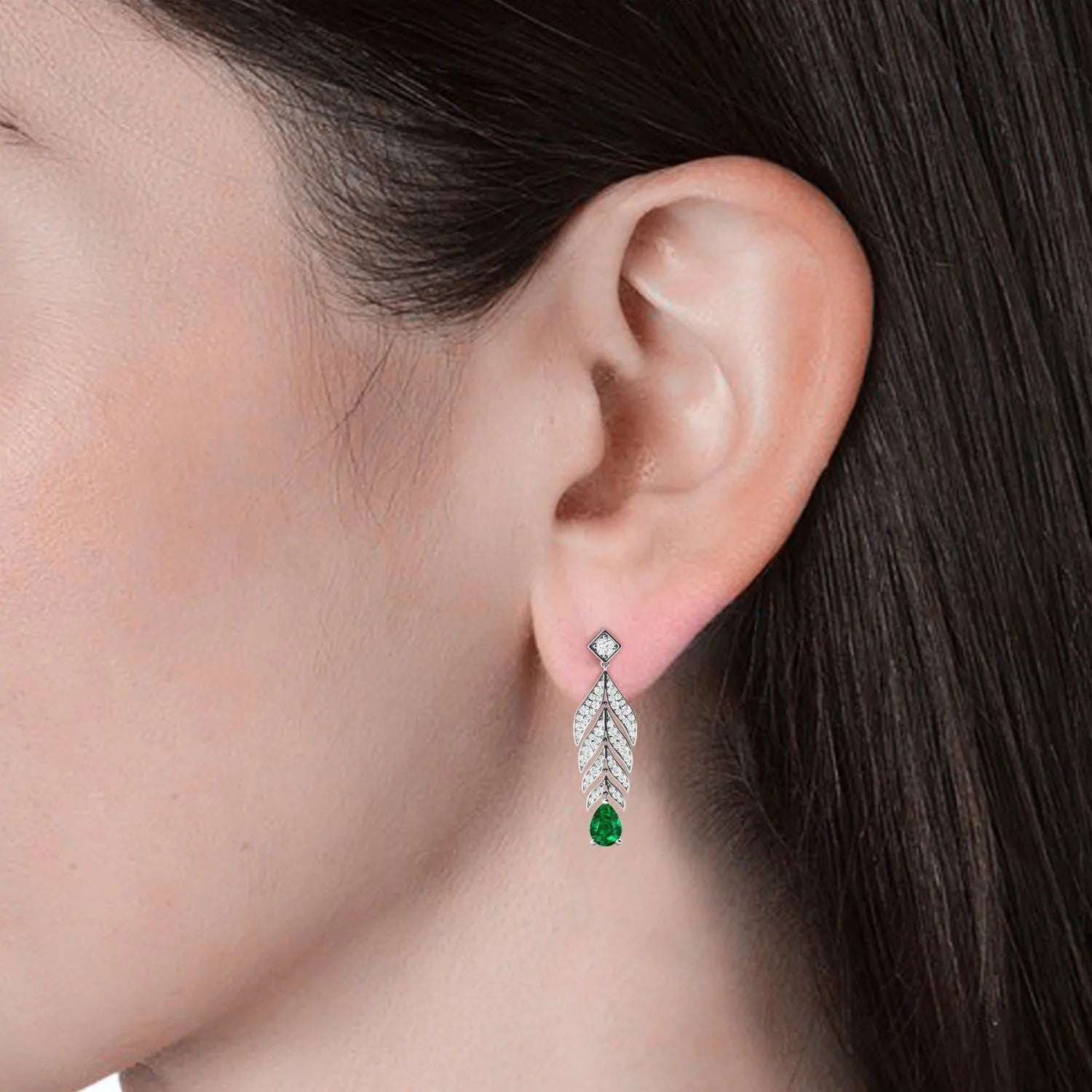 Close-up of a model’s ear wearing the feather-inspired emerald drop earrings.