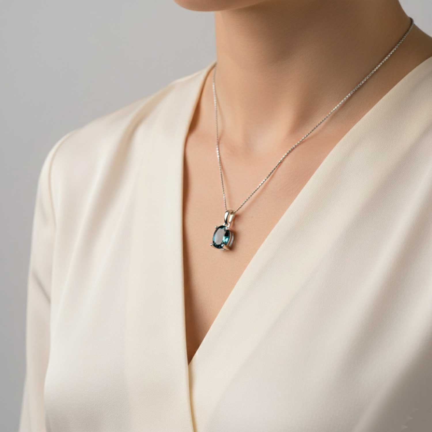 Necklace with a london blue topaz pendant worn by a person in a beige outfit against a neutral background