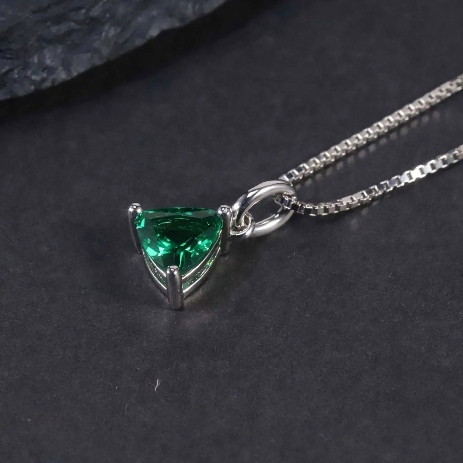 Close-up of the trillion-cut emerald pendant necklace displayed on a dark surface.