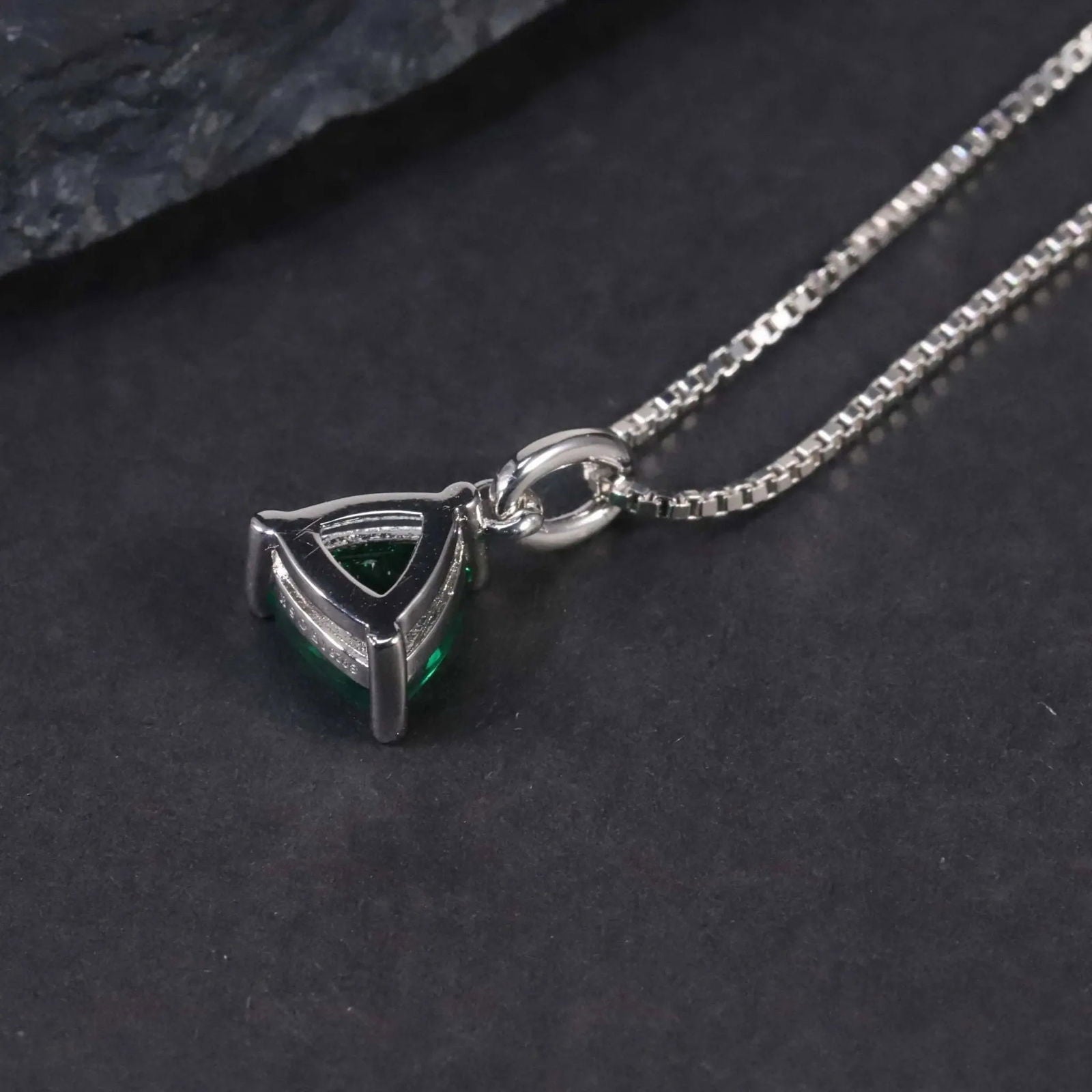 Alternate angle showing the trillion-cut emerald pendant necklace against a dark surface.
