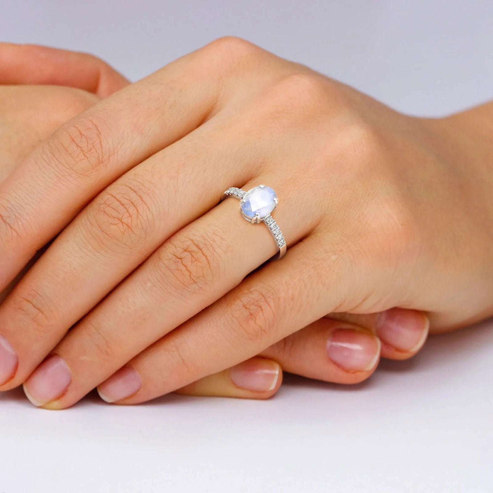 Model hand wearing the oval moonstone ring, showcasing its luminous centre stone and delicate band shimmer
