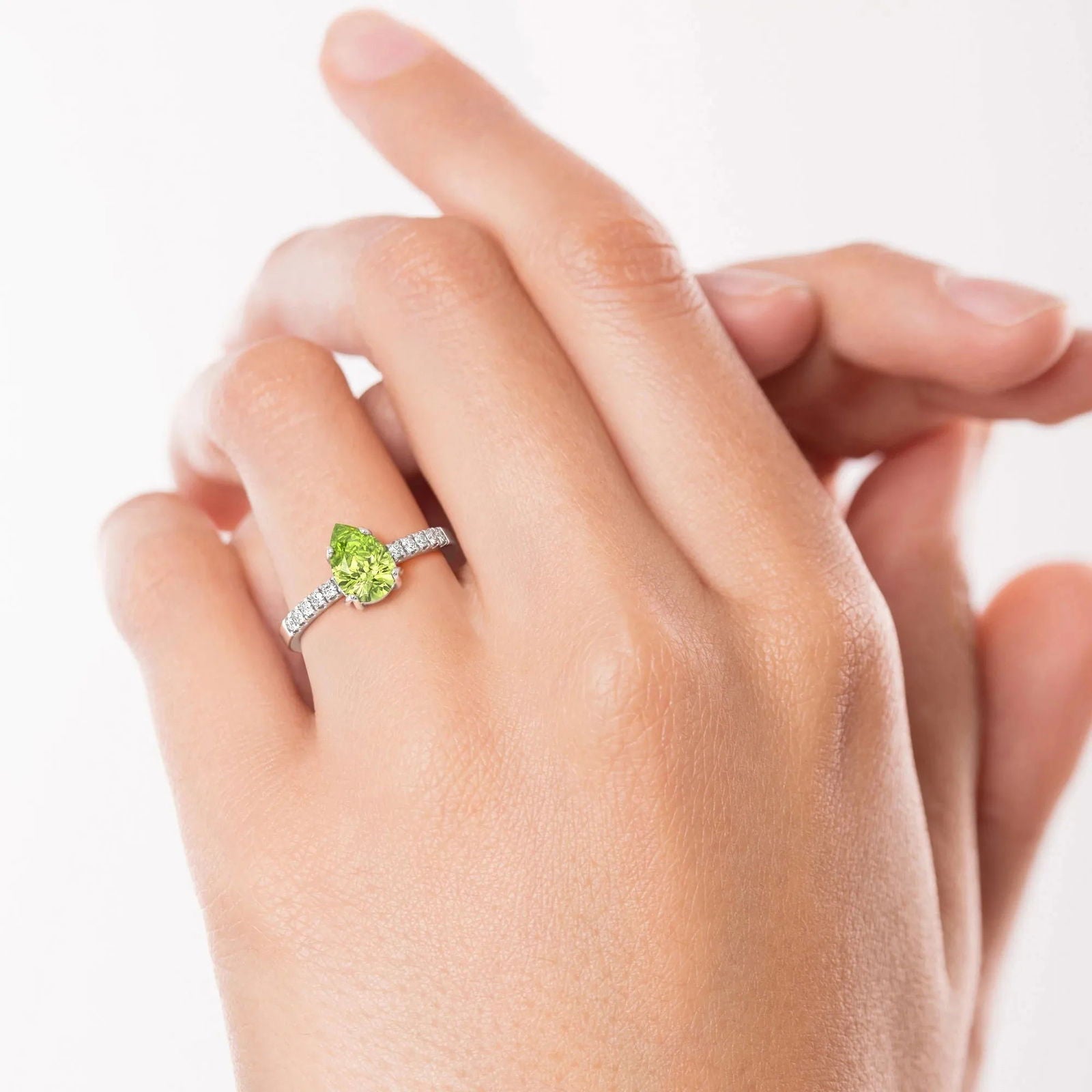 Hand wearing a sparkling Pear Cut Peridot Ring, highlighting the gemstone's brilliance and elegant band adorned with side stones.