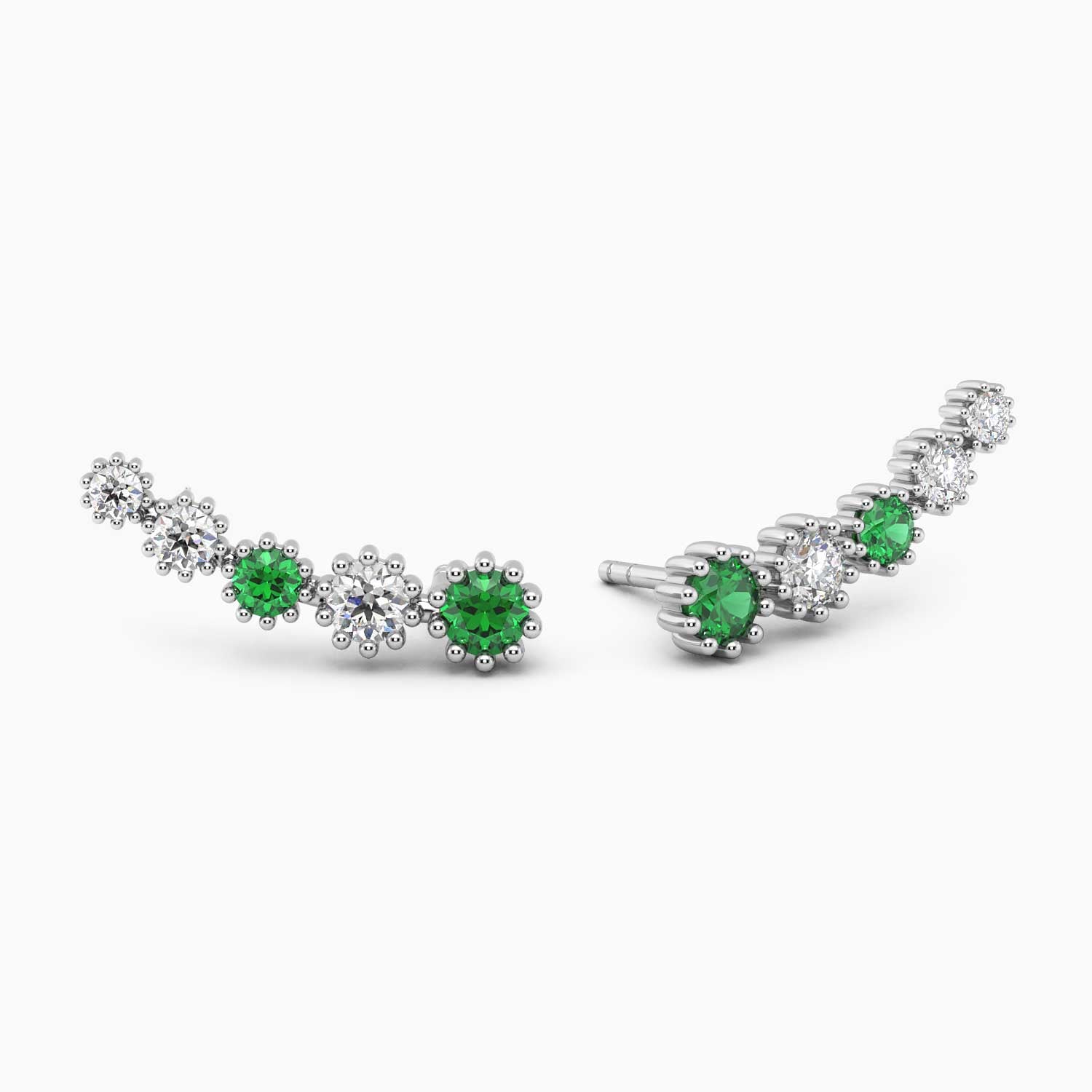 Angled view of the emerald climber earrings laid out, showing their prong settings and floral pattern.