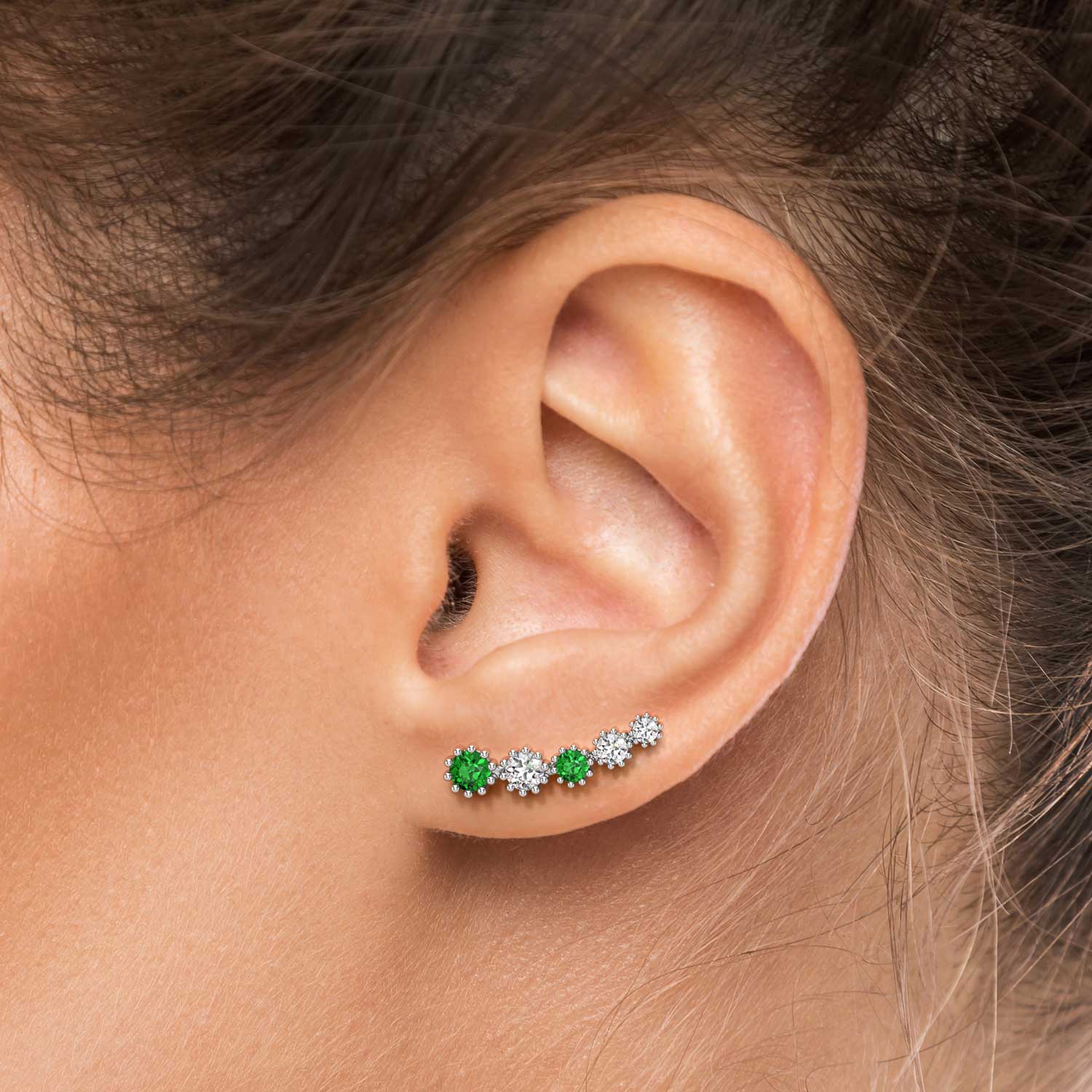Angled view of the emerald climber earrings laid out, showing their prong settings and floral pattern.