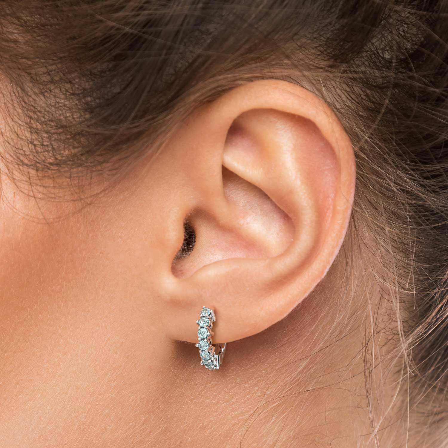 Close-up of a woman’s ear wearing an aquamarine huggie earring.