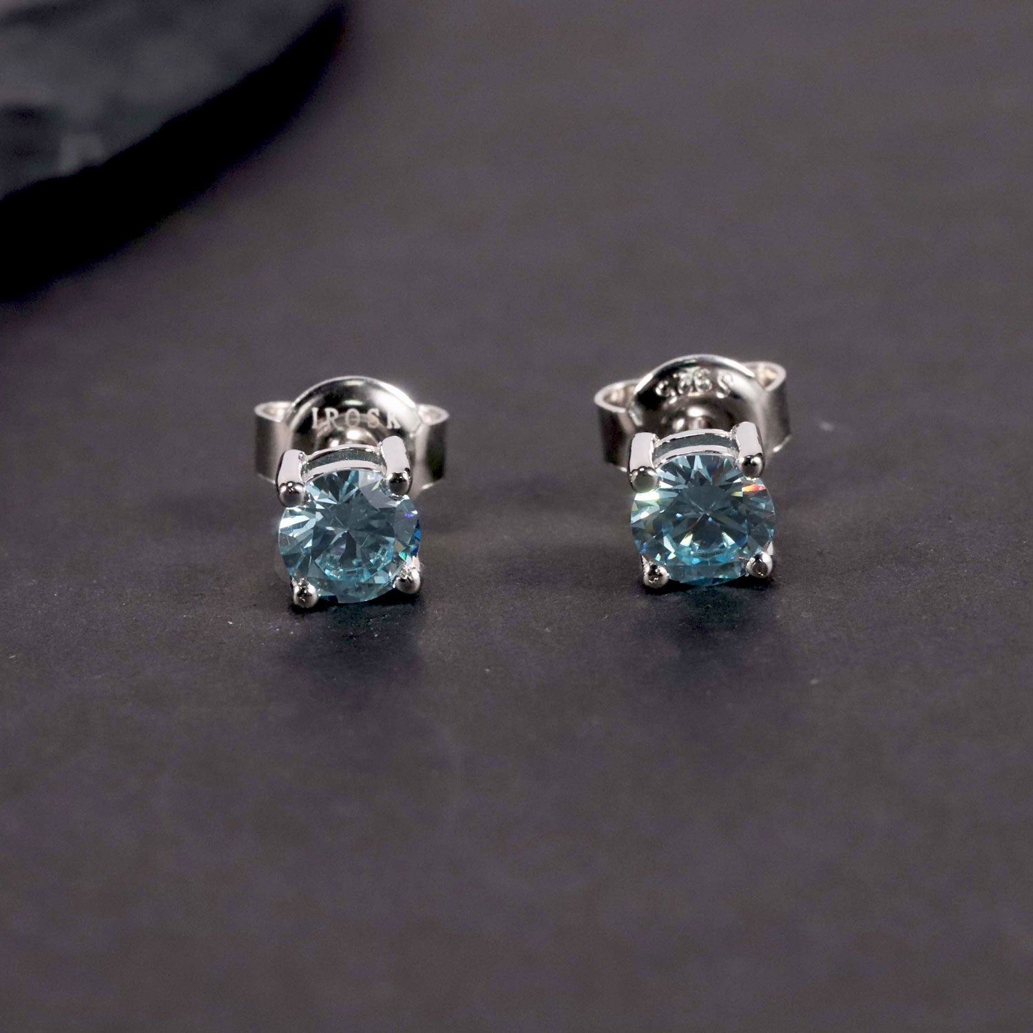front view of aquamarine round shape studs in silver in comparison with dark background