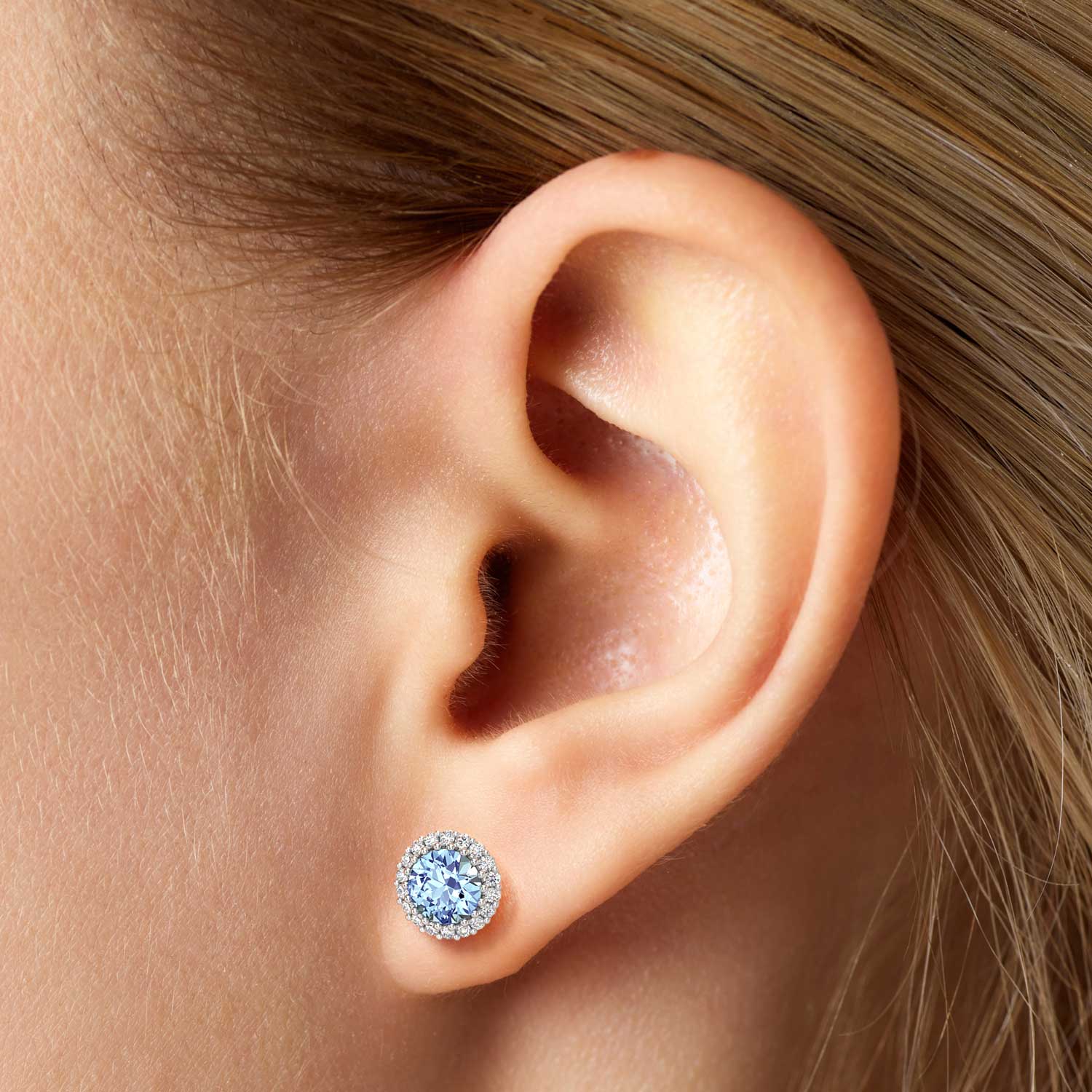 A close-up of a woman’s ear wearing a single aquamarine halo stud earring.