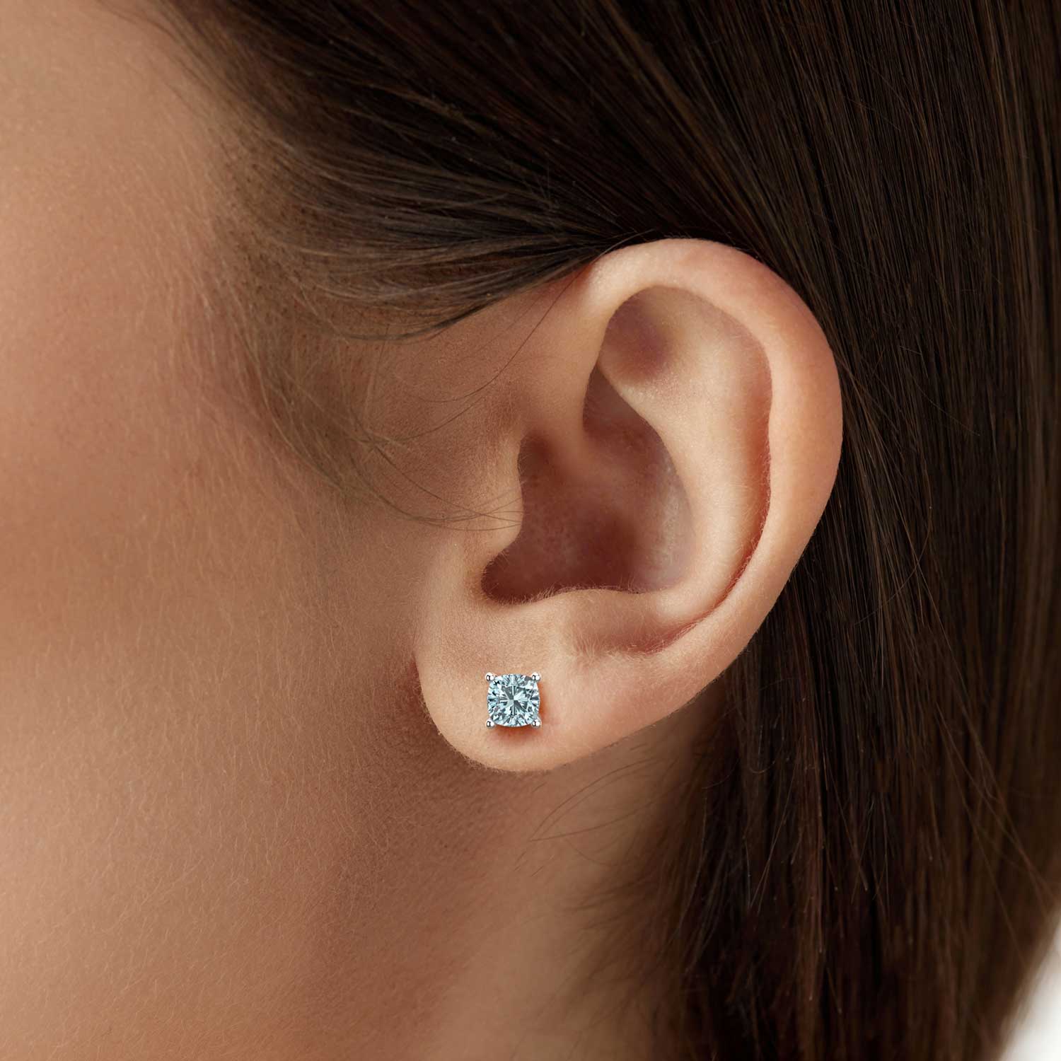 Close-up of a woman’s ear wearing a 6×6 mm cushion-cut aqua stud earring in a 925 sterling silver four-prong setting.