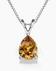 A pear-shaped golden citrine pendant in a three-prong sterling silver setting with a V-shaped bail, hanging from a delicate silver box chain on a white background; the gemstone displays warm amber and honey tones.