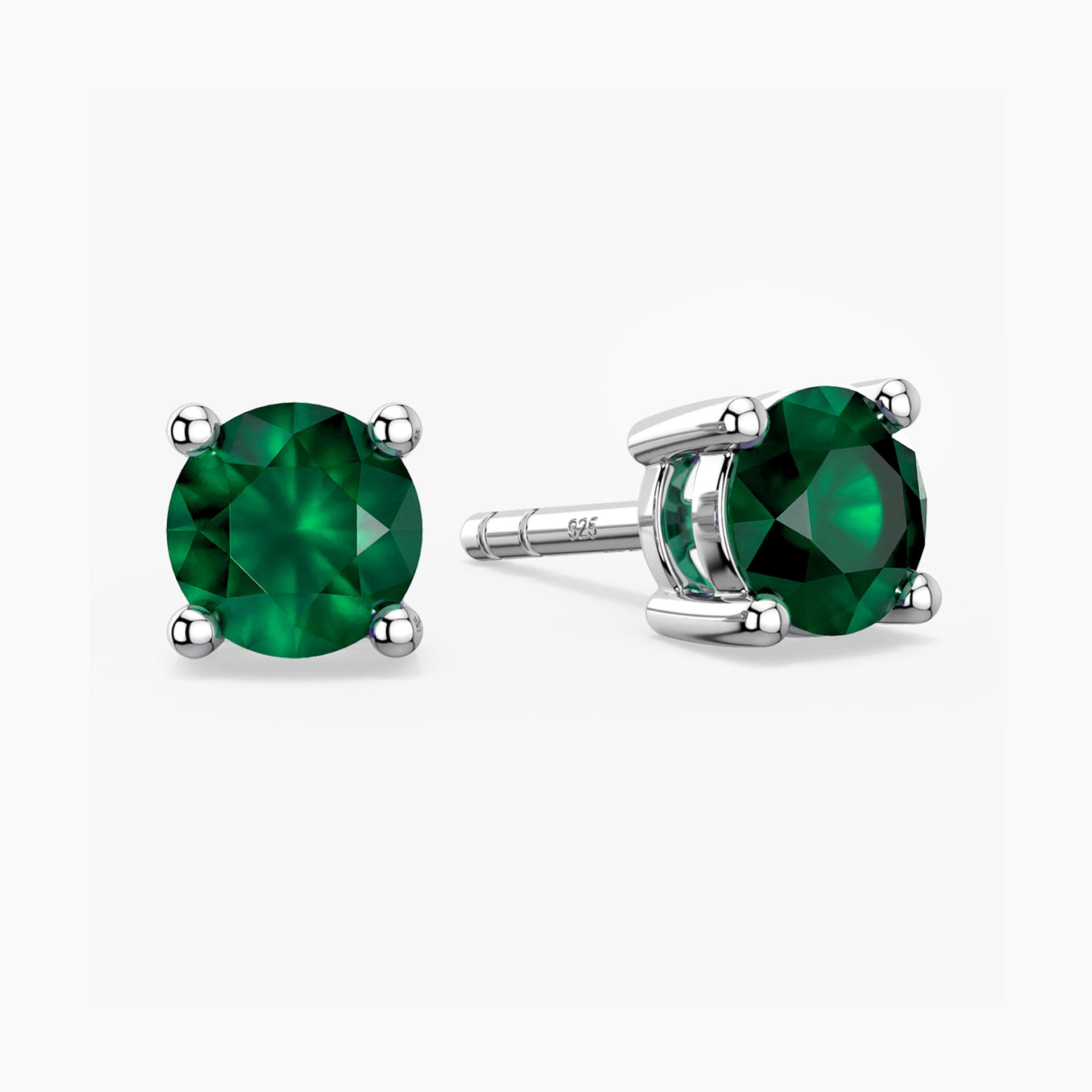 Sterling-silver stud earrings featuring round, faceted green emerald gemstones—one shown from the front and the other angled to reveal the four-prong setting and ‘S925’ hallmark on the post—against a white background.