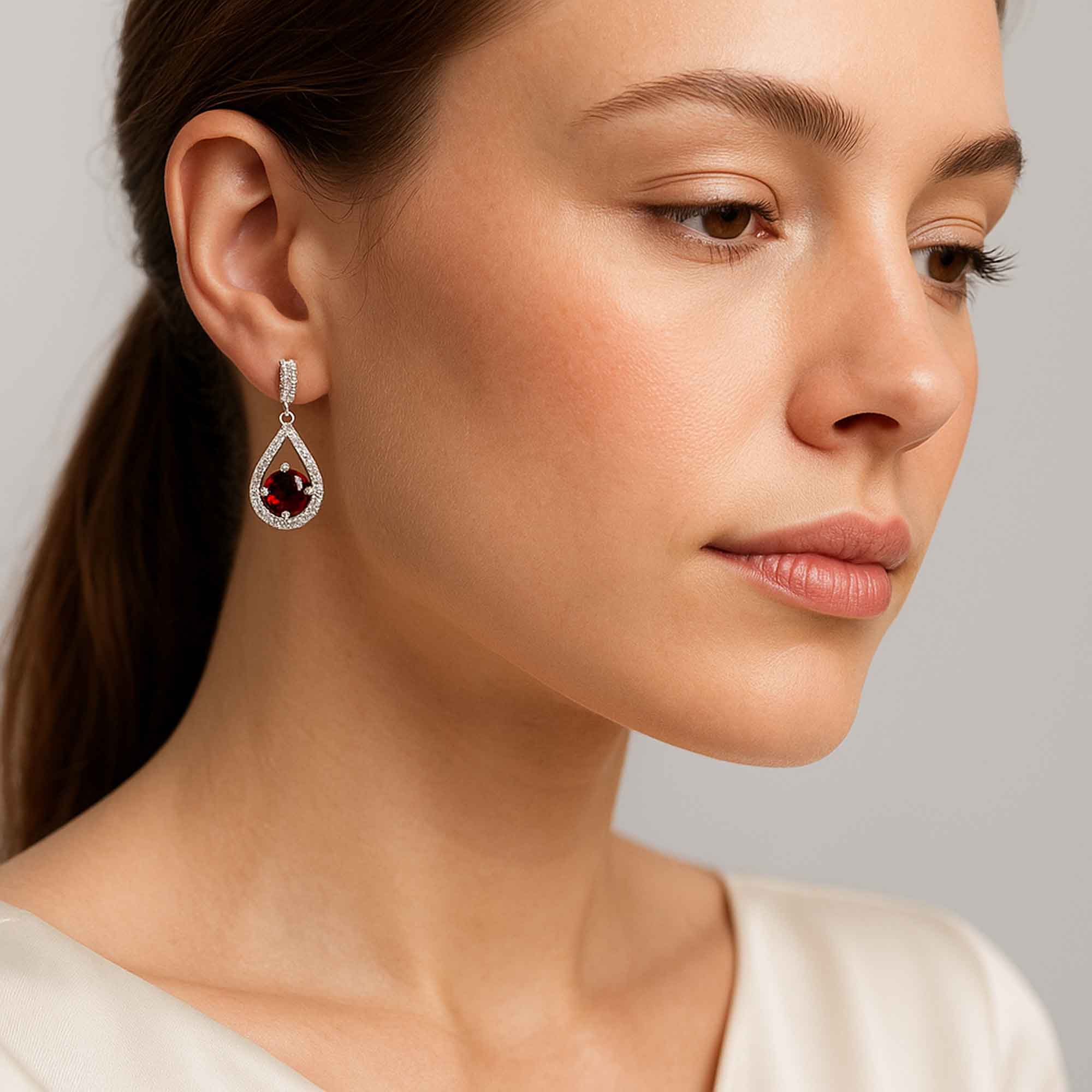 Close-up of a woman wearing a teardrop garnet earring with a red gemstone on a neutral background