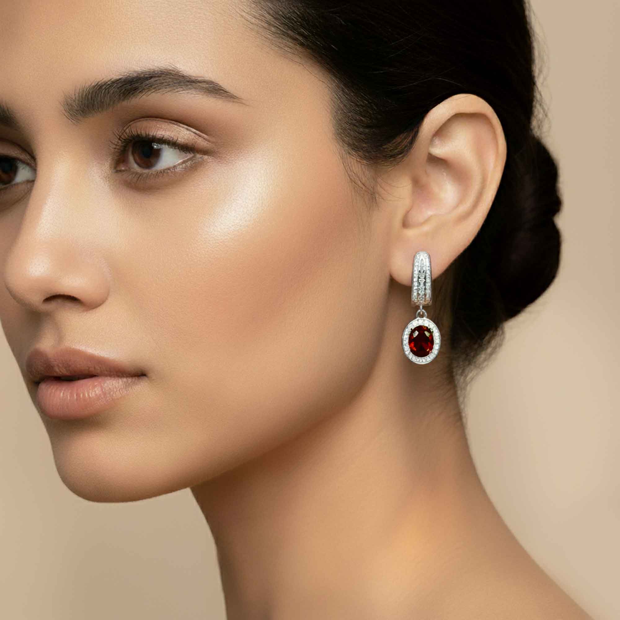 Close-up of a woman wearing a silver earring with a red garnet gemstone on a beige background