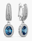 Pair of earrings with london blue topaz gemstones and silver accents on a white background