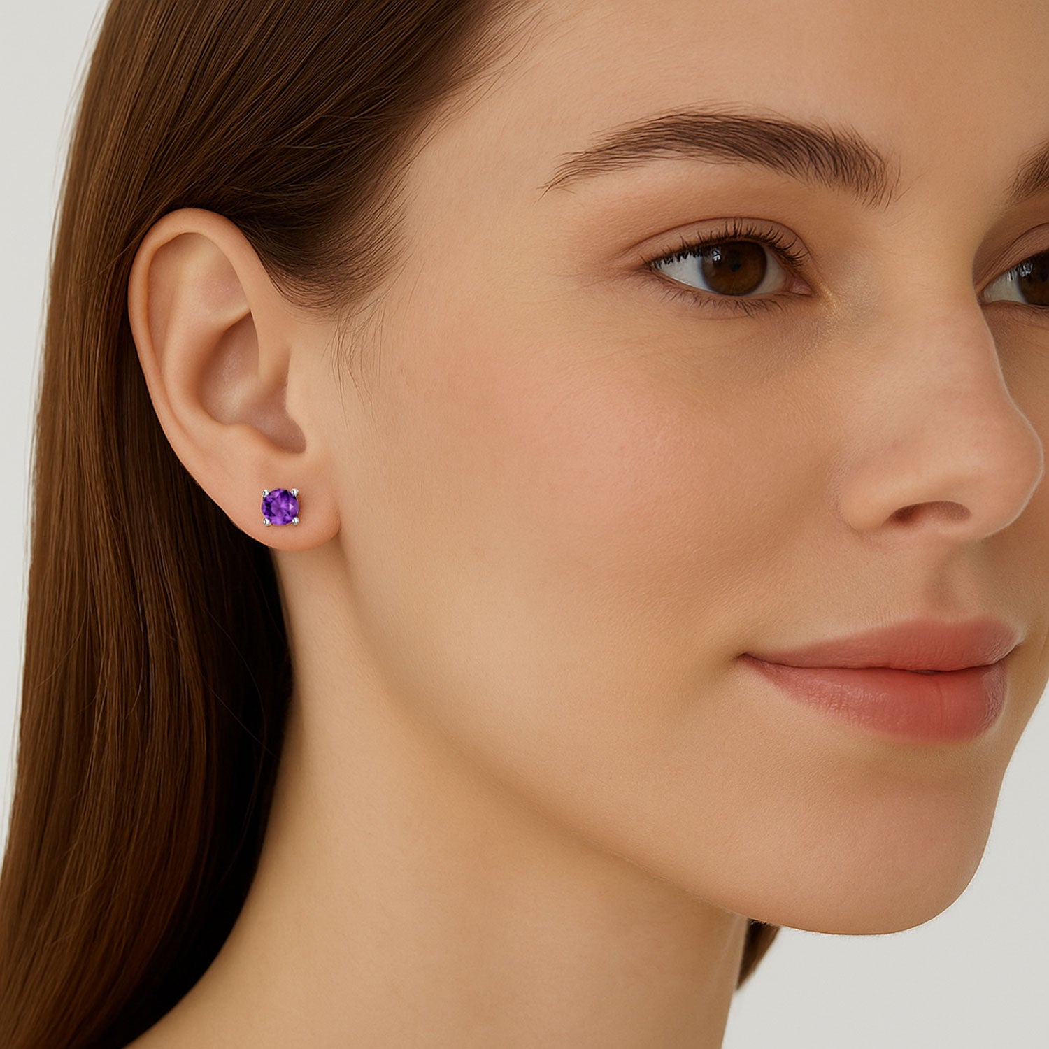 Close-up of a woman wearing a purple amethyst gemstone earring on a plain background