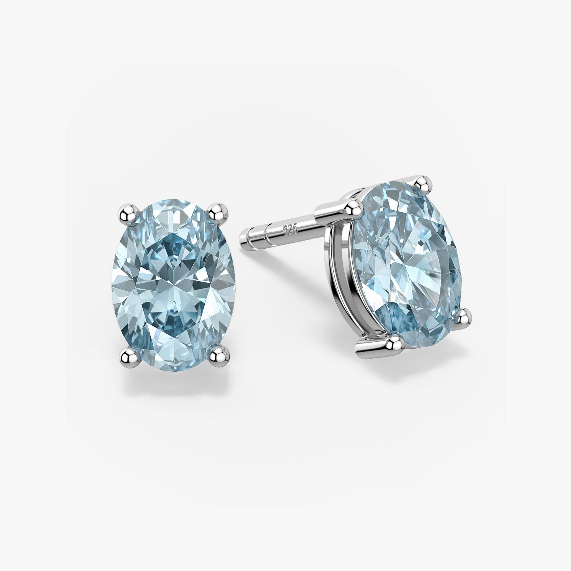 Pair of oval-cut light blue aquamarine stud earrings in a four-prong silver setting with push-back closures, displayed on a white background.