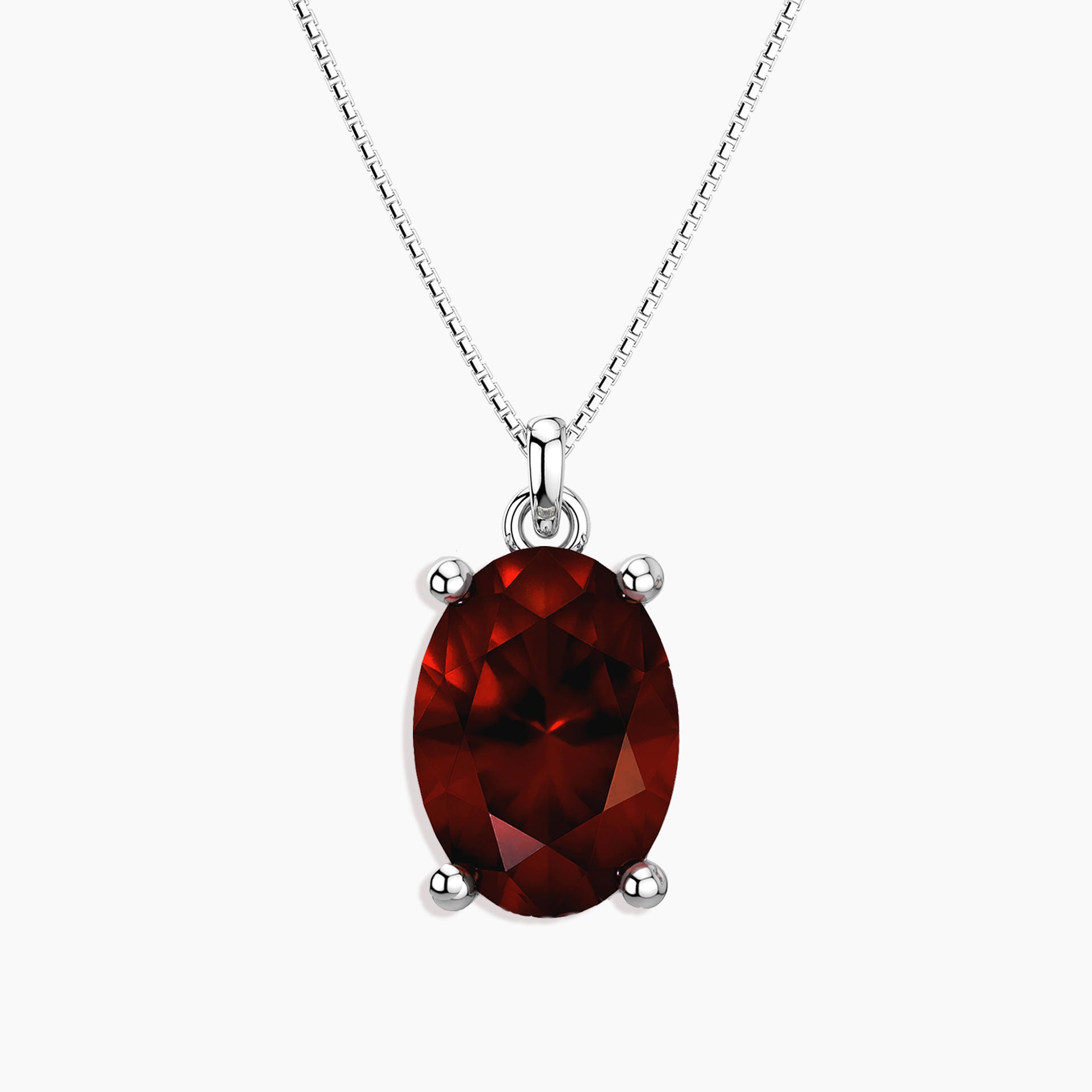 Oval-cut deep red garnet pendant in a four-prong silver setting, hanging from a silver box chain necklace, displayed on a white background