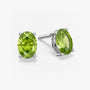 Pair of oval-cut green peridot stud earrings in a four-prong silver setting with push-back closures, displayed on a white background.