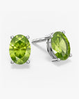 Pair of oval-cut green peridot stud earrings in a four-prong silver setting with push-back closures, displayed on a white background.