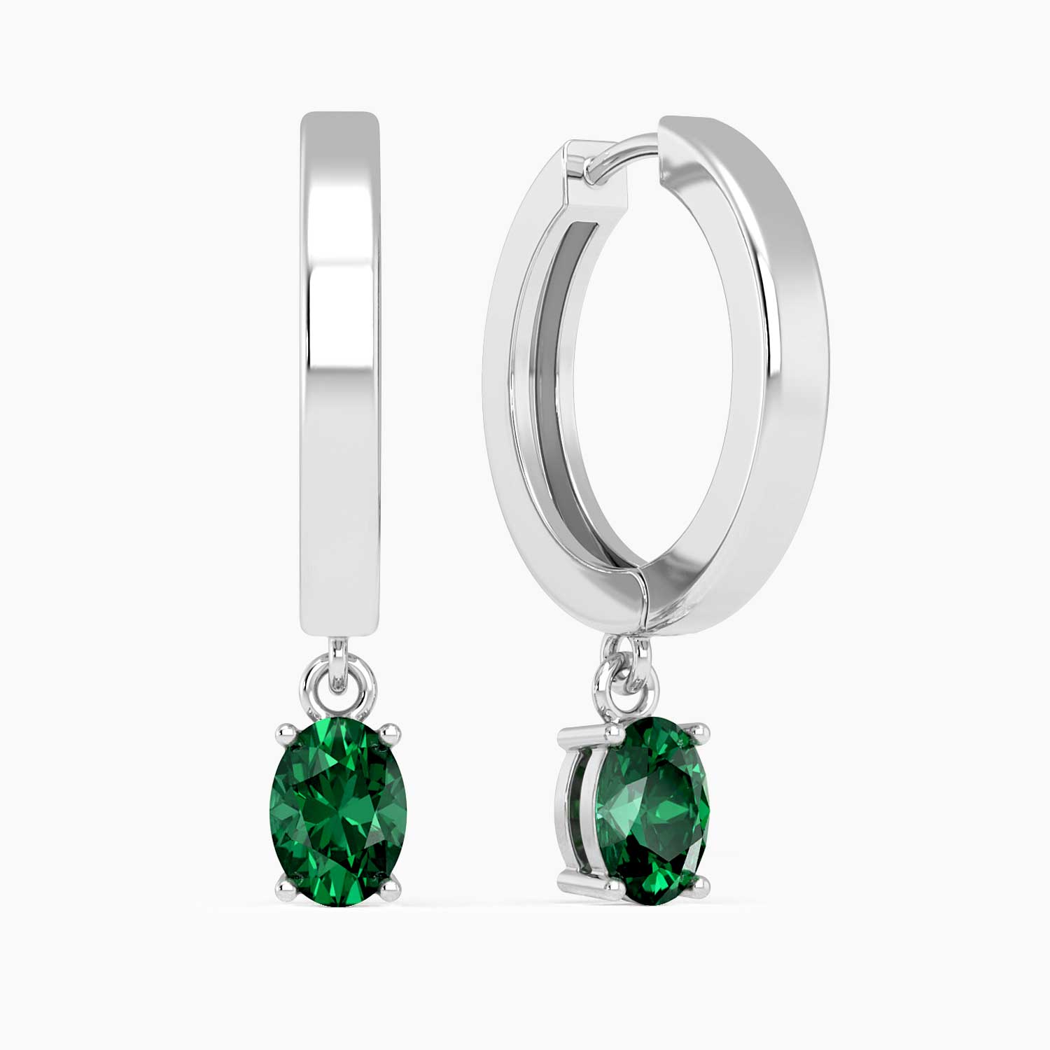 Close-up of silver hoop earrings with oval emerald drops, showcasing their polished finish and vibrant green gemstones.