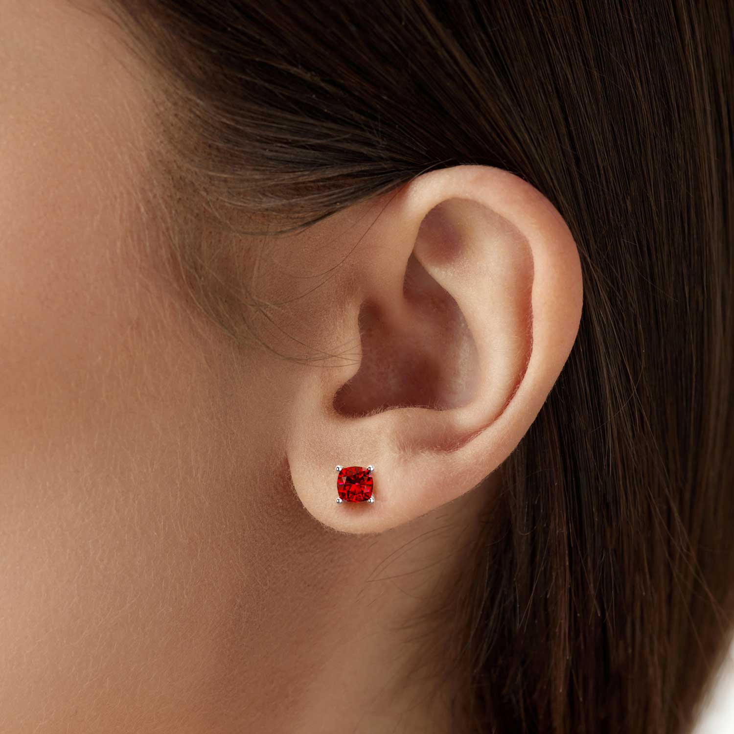 Close-up of an ear wearing a cushion-cut ruby stud earring in a 925 sterling silver four-prong setting