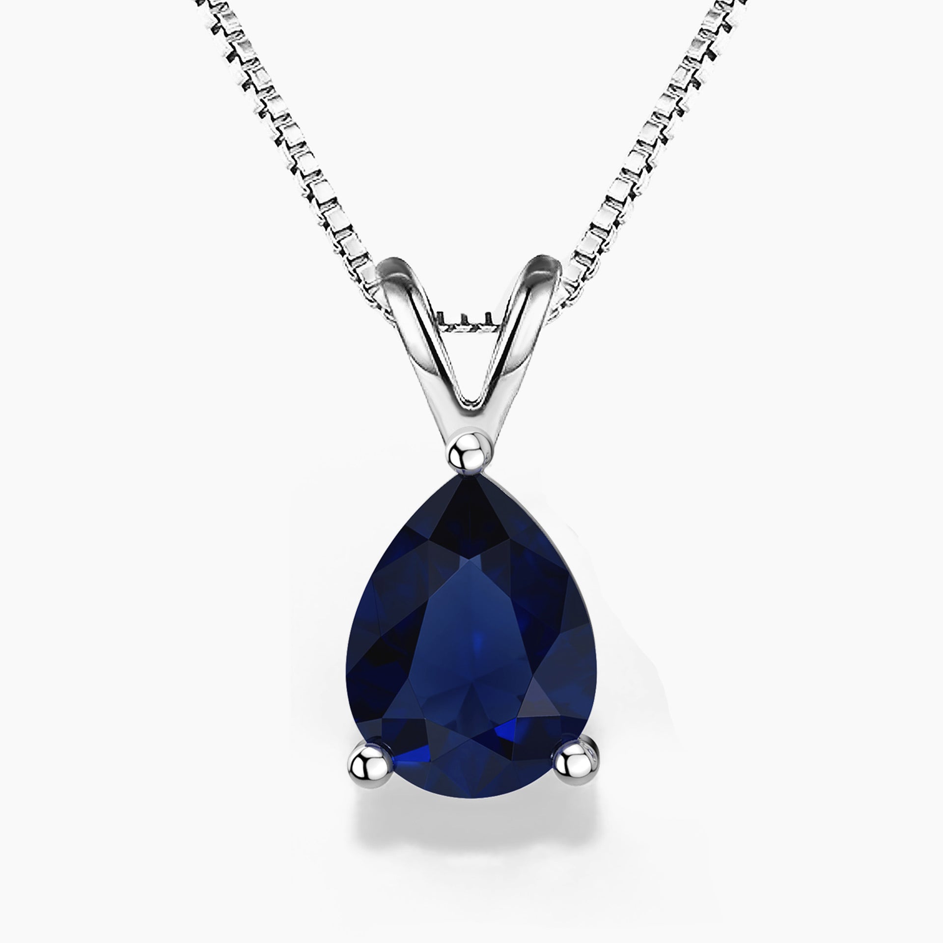 Alt: A pear-shaped deep-blue sapphire gemstone pendant in a sleek three-prong sterling silver setting, hanging from a delicate silver box chain with a V-shaped bail on a white background.