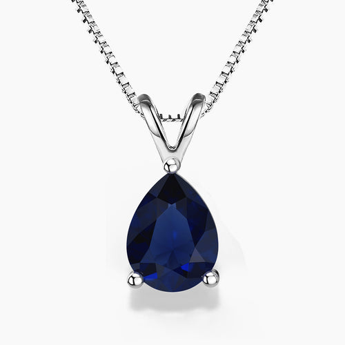 Alt: A pear-shaped deep-blue sapphire gemstone pendant in a sleek three-prong sterling silver setting, hanging from a delicate silver box chain with a V-shaped bail on a white background.