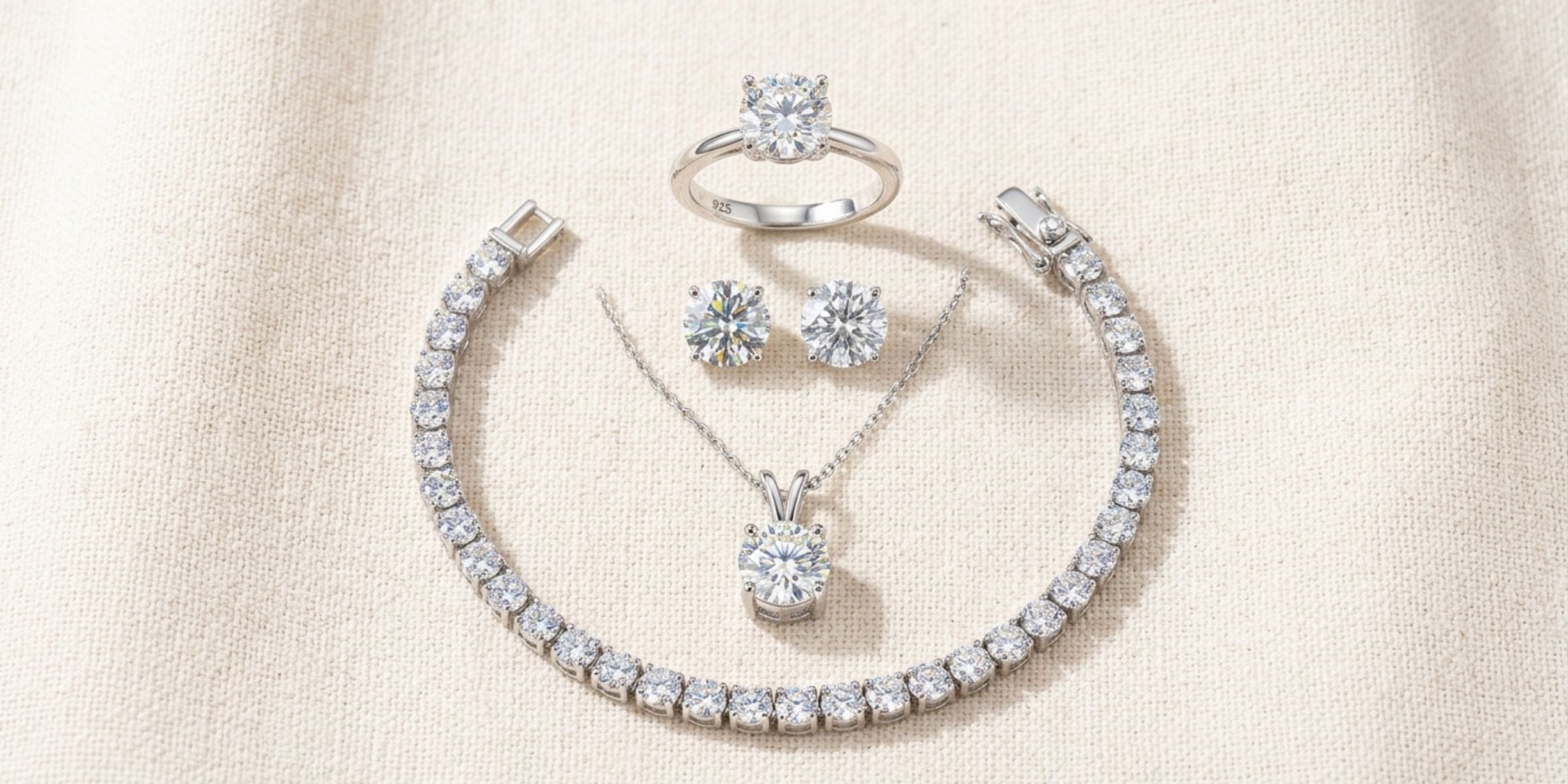 Flat-lay of sterling silver moissanite ring, necklace, earrings and tennis bracelet