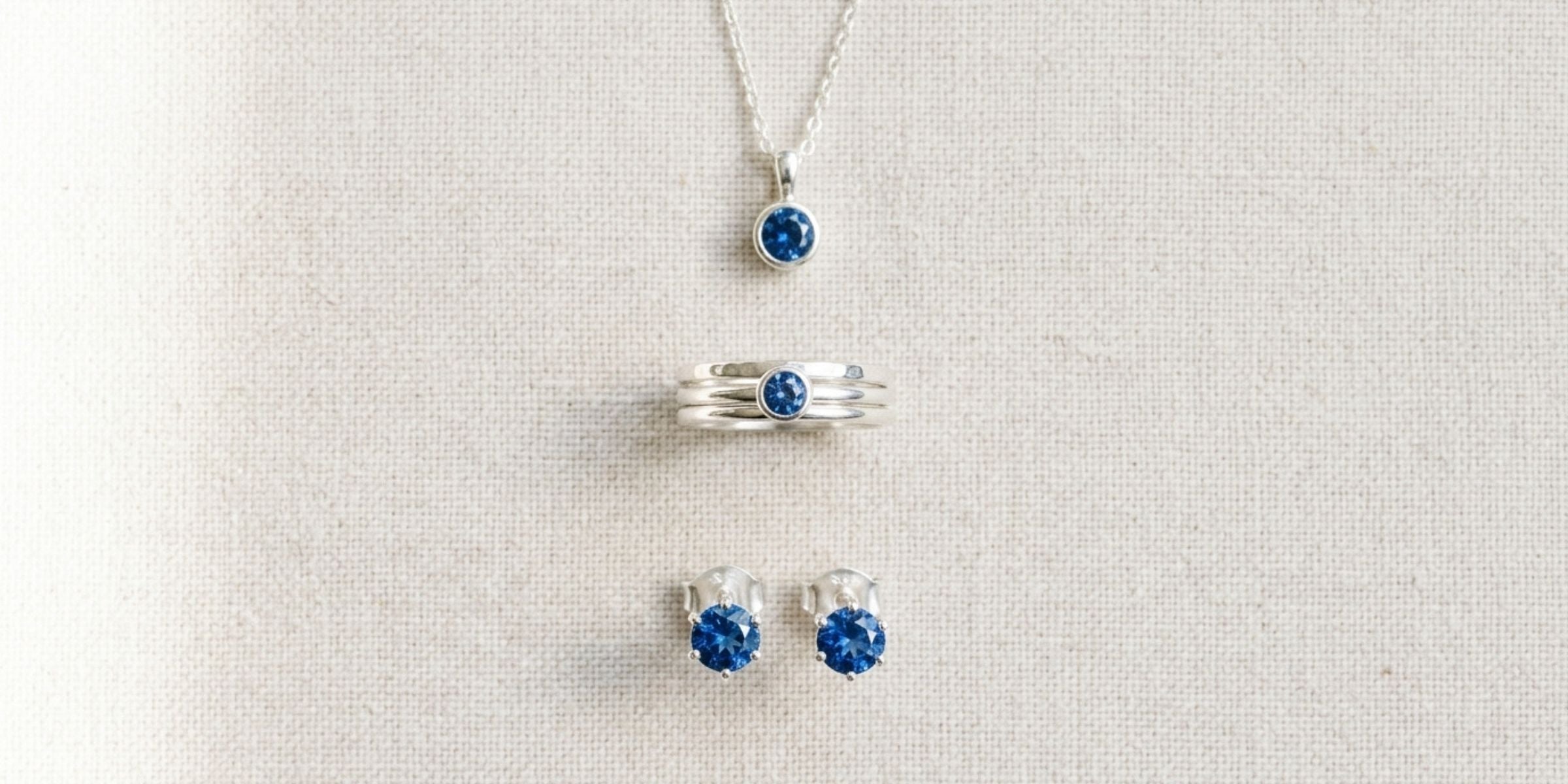 Loose blue sapphire gemstone beside a sterling silver sapphire pendant on silk