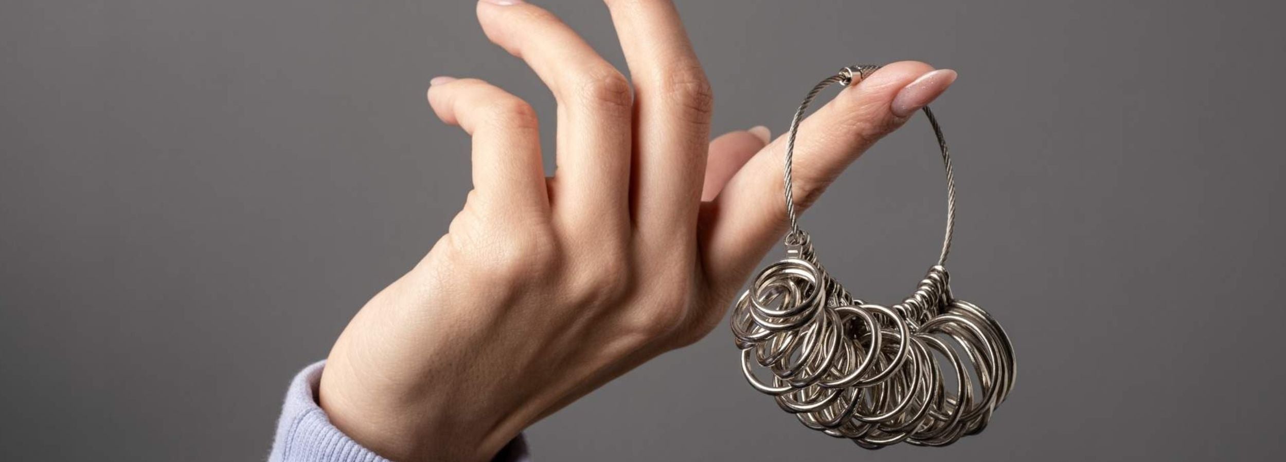 Hand holding a silver hoop earring against a gray background