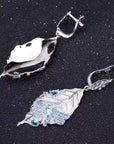 Silver leaf-shaped earrings with blue gemstones on a dark background