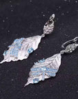Silver leaf-shaped earrings with blue gemstones on a black background