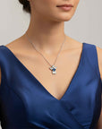Woman wearing a blue dress with a silver necklace featuring a blue topaz gemstone pendant.