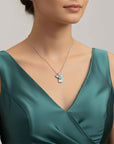 Woman wearing a green dress with a necklace featuring a blue aquamarine pendant.