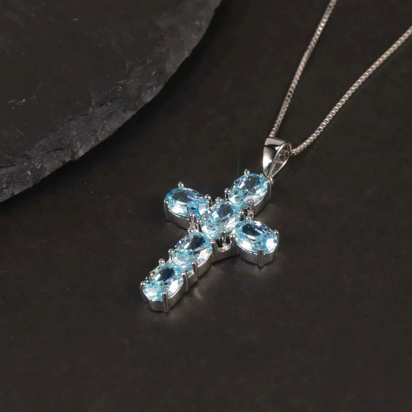 Close-up of the aquamarine cross pendant necklace on a black background, highlighting its gemstones and silver setting.