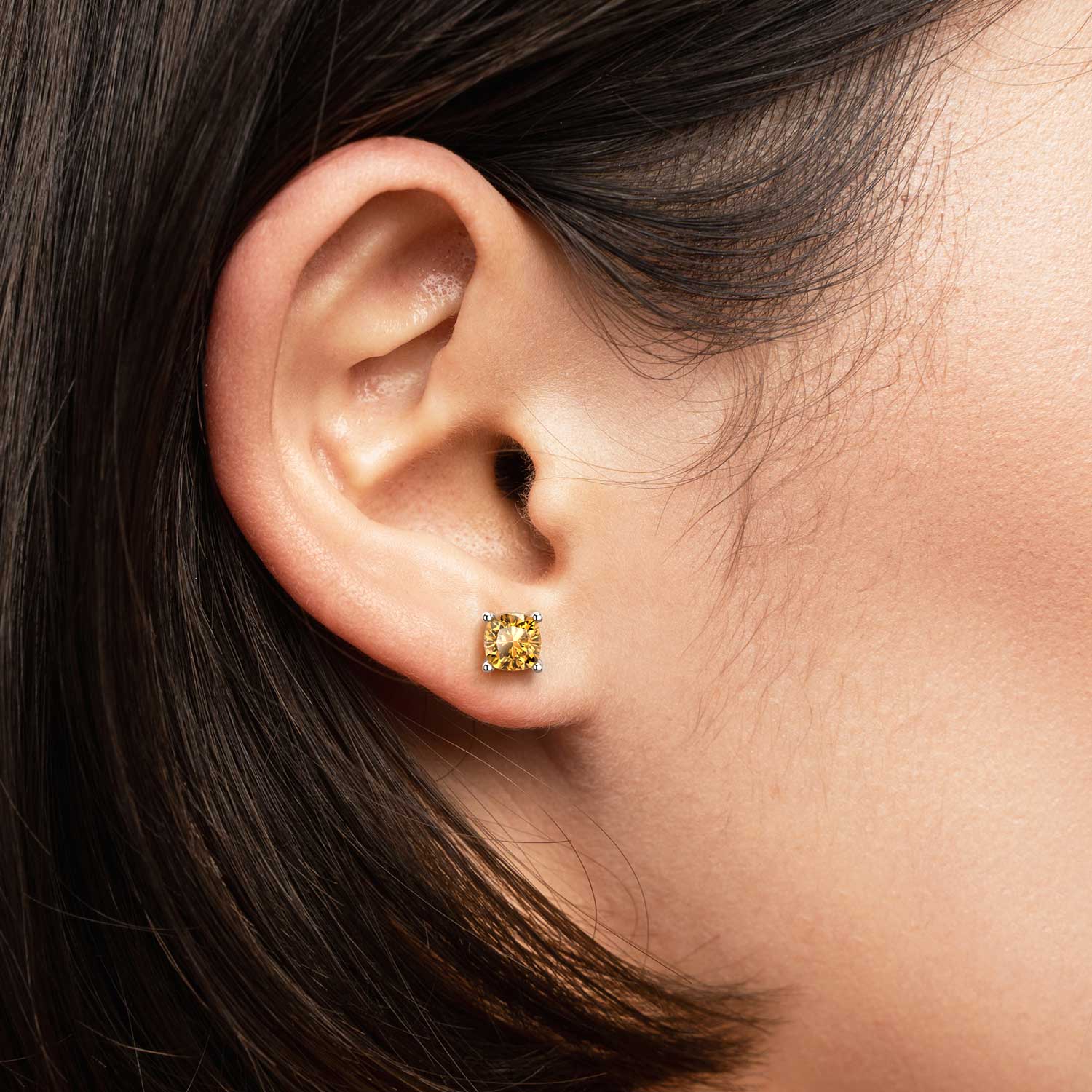 Close-up of a woman’s ear wearing a 6×6 mm cushion-cut citrine stud earring in a sterling silver four-prong setting.