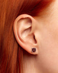 Close-up of a woman’s ear wearing a 6×6 mm cushion-cut garnet stud earring in a 925 sterling silver four-prong setting.