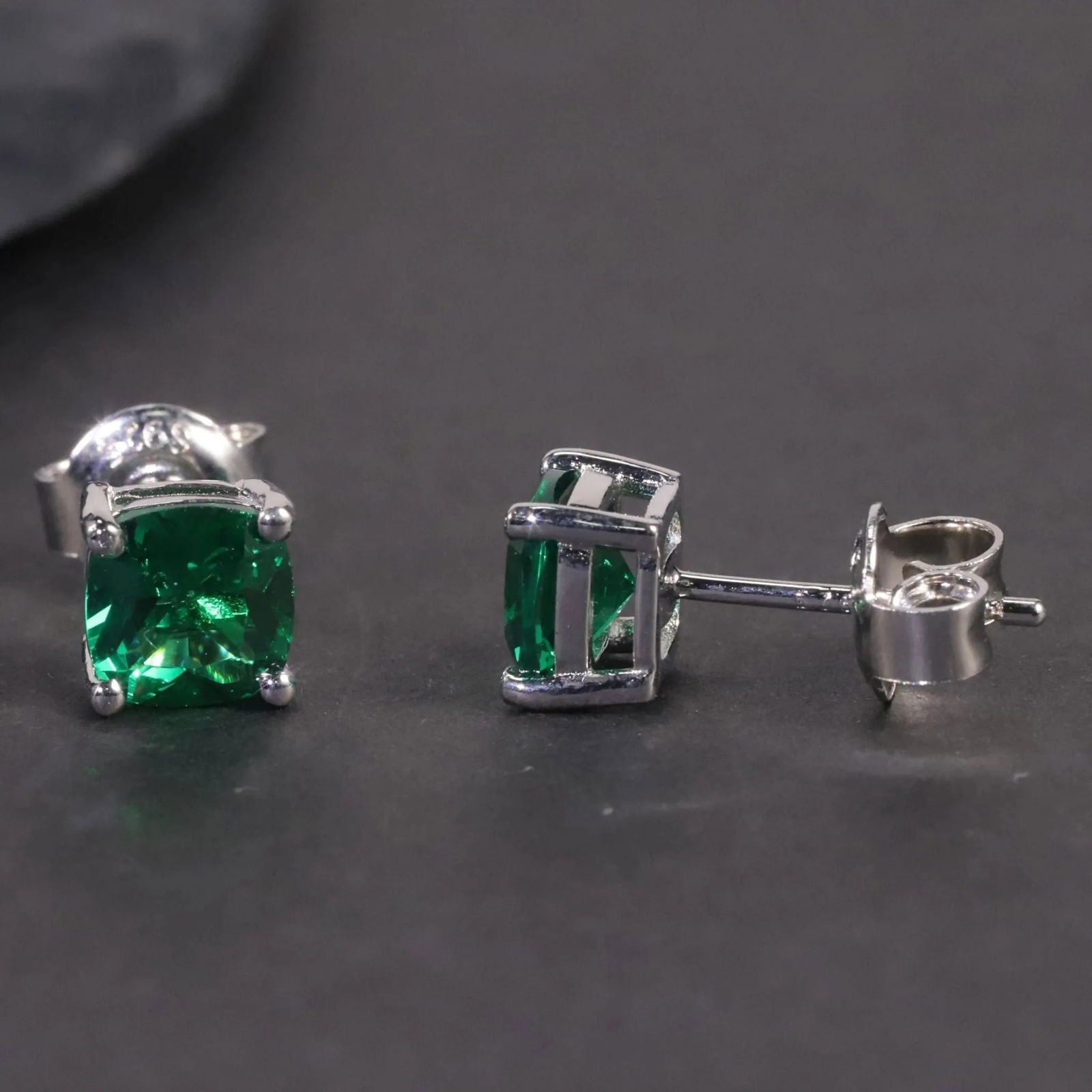 Alternate angle showing the cushion-cut emerald stud earrings against a dark surface.