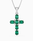 Sterling silver cross pendant with six oval emeralds displayed against a dark background.