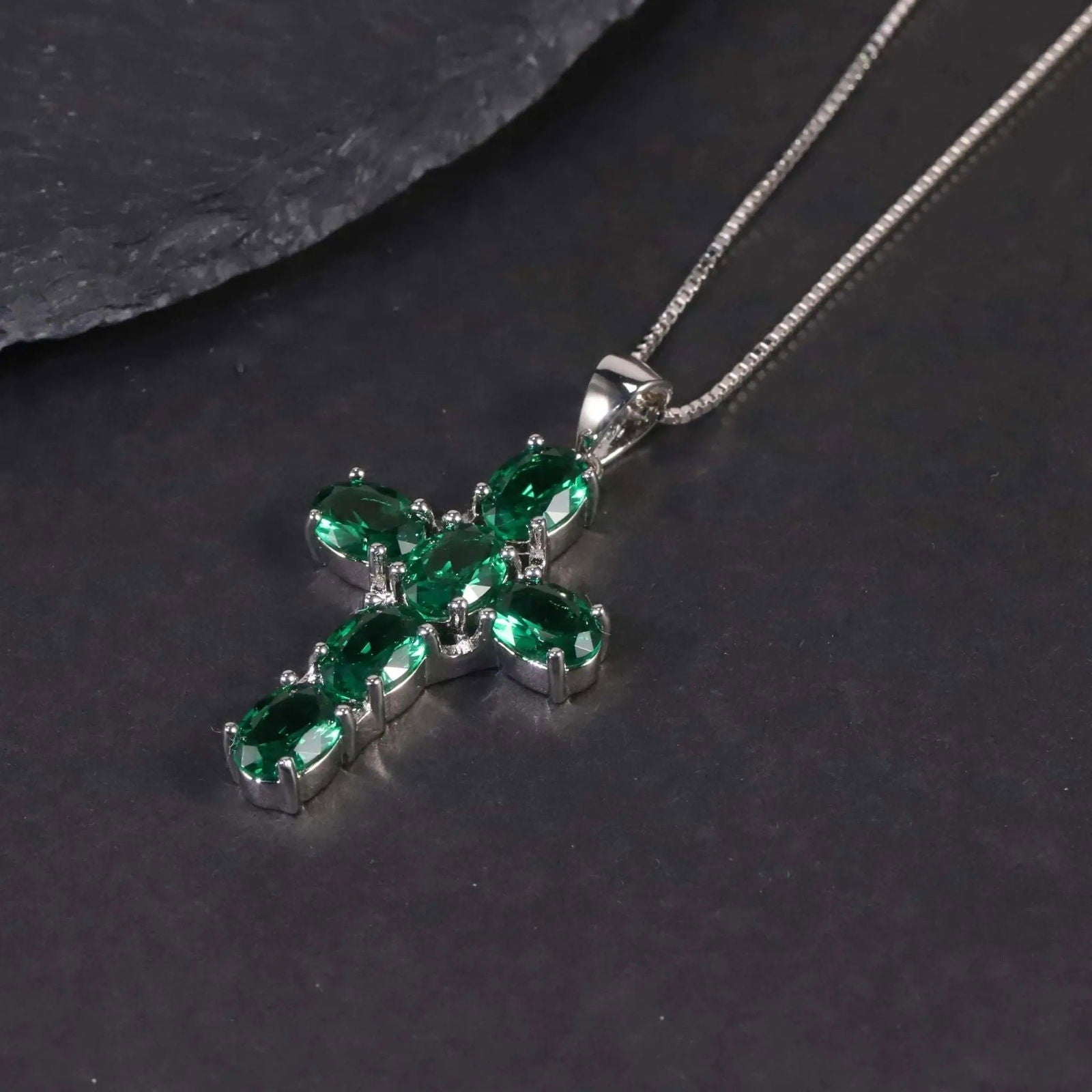 Close-up of the oval emerald cross pendant resting on a dark surface.