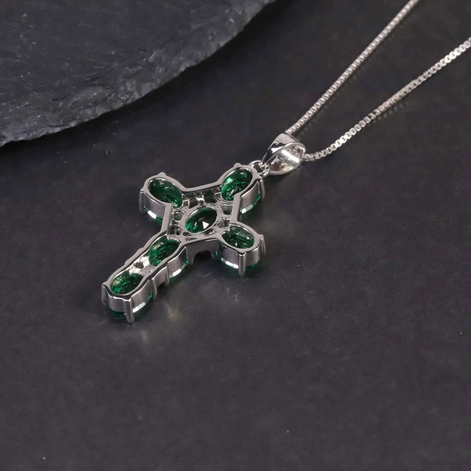 Alternate angle showing the emerald cross pendant against a dark surface.