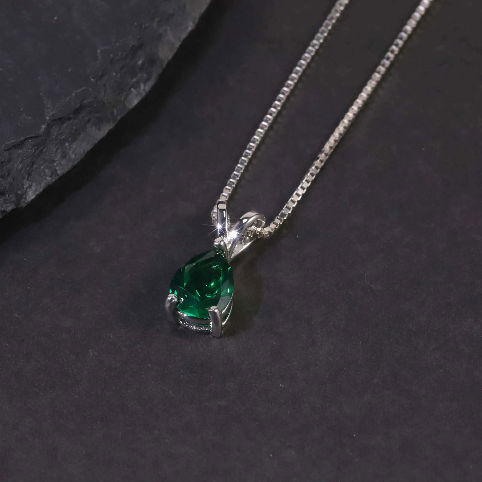 Close-up of the pear emerald pendant necklace displayed on a dark surface.