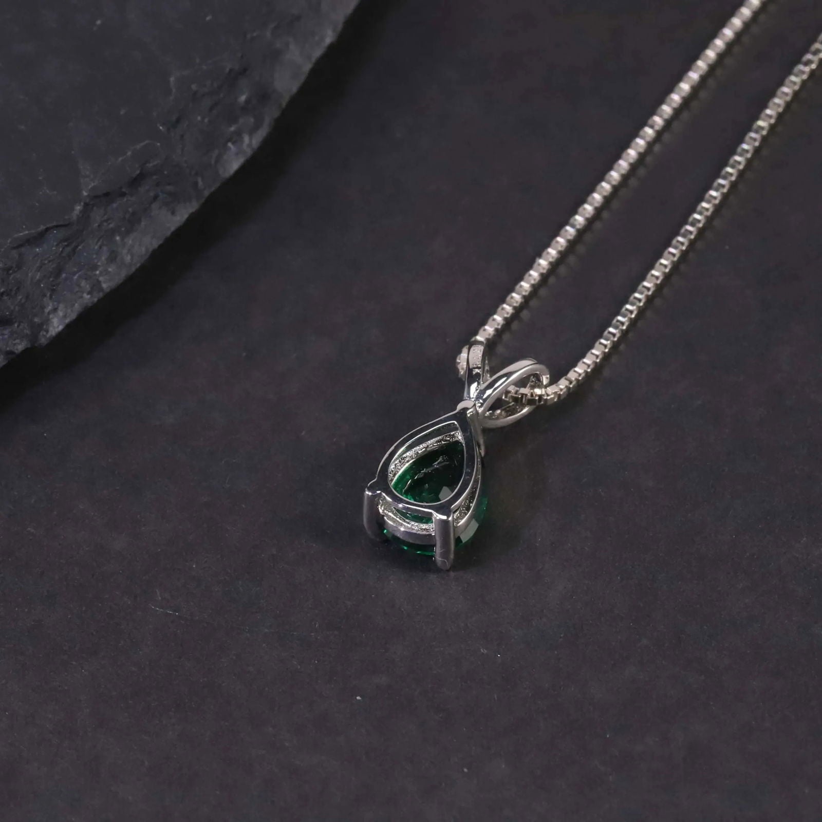 Alternate angle of the pear emerald pendant necklace against a dark surface.