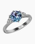 Angled side view of round Alexandrite trilogy ring with side cubic zirconia and rhodium-plated finish