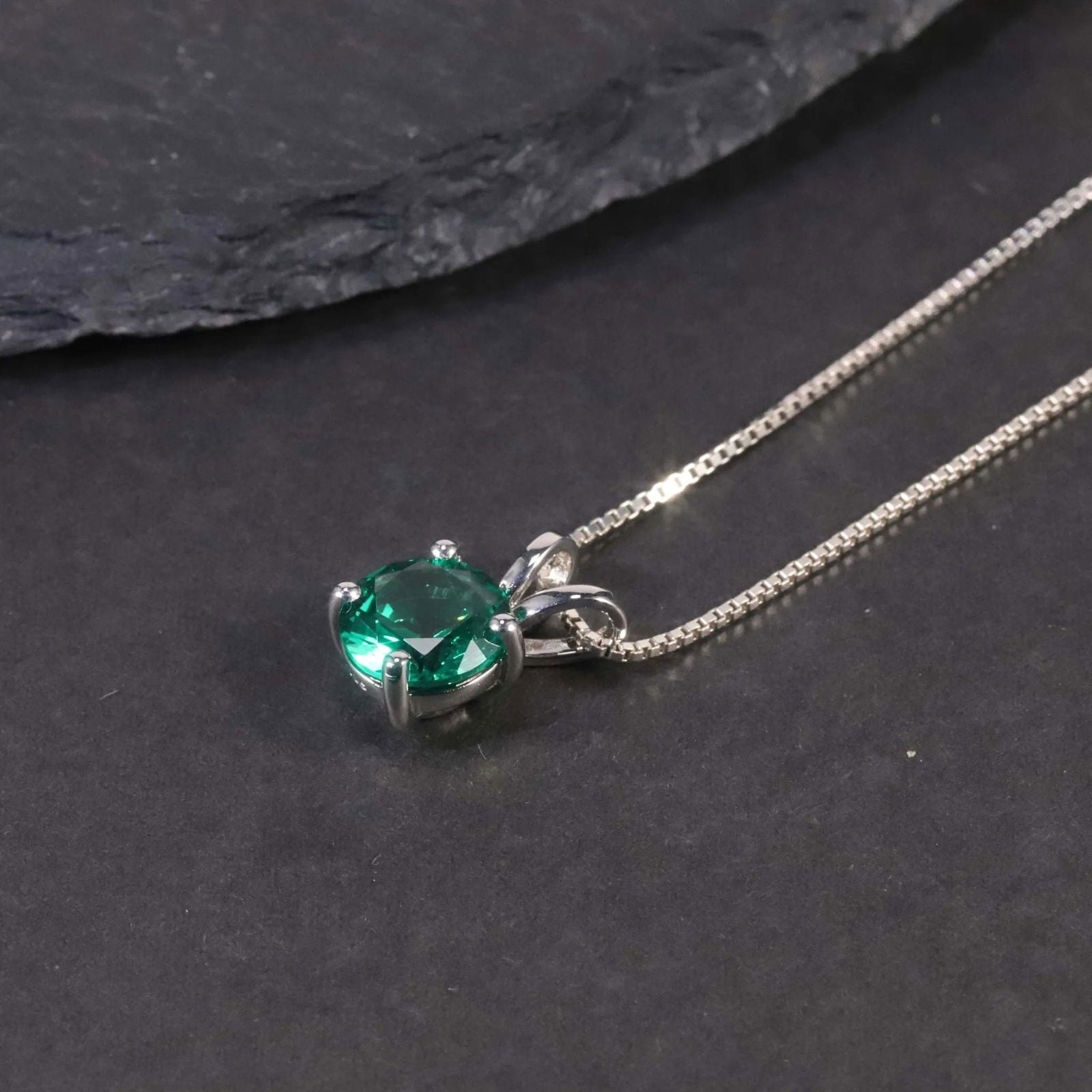 Close-up of the round emerald pendant necklace displayed on a dark surface.