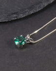 Close-up of the round emerald pendant necklace displayed on a dark surface.